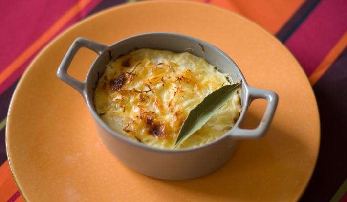 Fotografia de um recipiente pequeno que foi ao forno com uma receita de chuchu recheado com creme de milho e frango. A receita foi gratinada e tem uma folha de louro por cima.