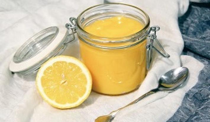 Foto da receita de Lemon Curd. Observa-se um potinho de vidro hermético com o creme de limão dentro e, ao lado esquerdo, um limão pela metade decora a foto.