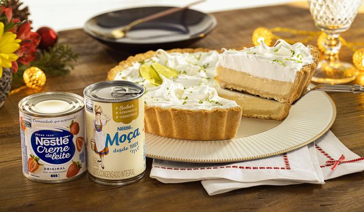 Imagem de uma torta de limão em um prato e uma fatia na espátula. Ao lado, uma lata de Creme de Leite Nestlé e Leite Moça.