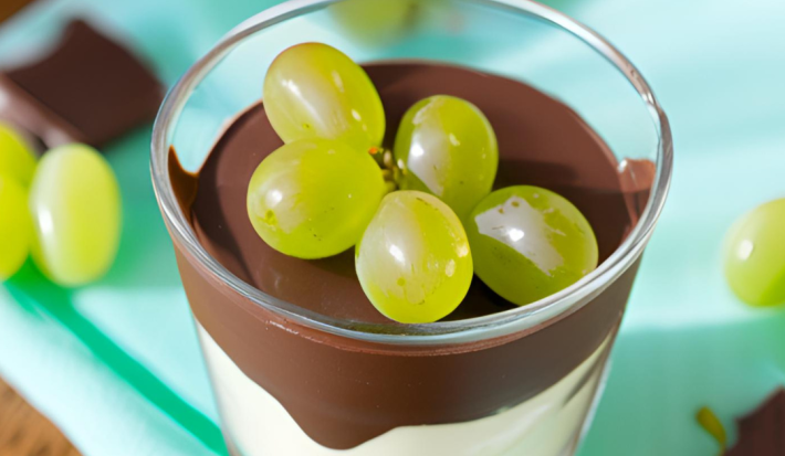 Foto da Receita de Bombom de Uva no Copo. Observa-se um copo de vidro com um creme baixo embaixo, por cima chocolate e decorado com uvas verdes. Foto gerada por IA.