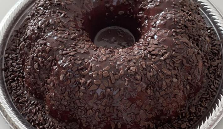 Foto em tons de marrom da receita de bolo cenourolate servida em uma porção grande sobre uma forma descartável branca