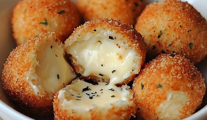 Fotografia de várias bolinhas de queijo crocantes dentro de um recipiente médio e fundo de cor branca. O foco da imagem mostra três metades abertas com o queijo derretido.