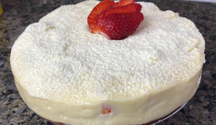 Fotografia em tons de cinza com um bolo de cobertura branca ao centro. Por cima da cobertura existe um polvilhado de Leite NINHO em pó e fatias de morango