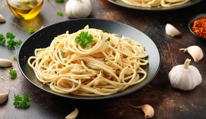 Imagem de um prato preto com macarrão alho e óleo decorado com salsinha.