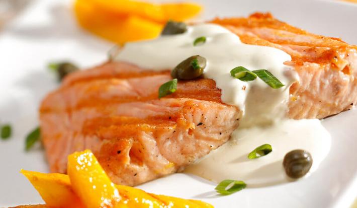 uma travessa branca contém um salmão com creme branco por cima e ao lado fatias de manga.