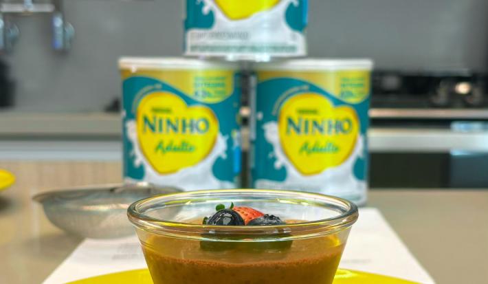 Fotografia em tons de amarelo com um potinho de vidro ao centro. Dentro do pote existe uma receita de mousse de chocolate com Ninho Adulto e chia