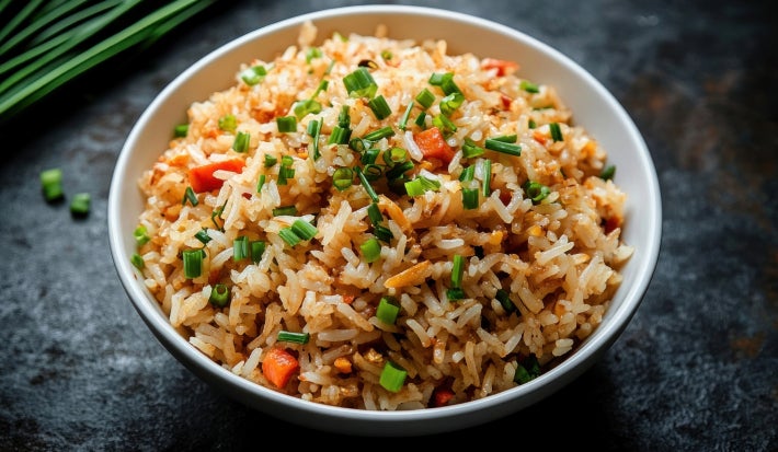 Fotografia em tons claros com um prato branco e fundo ao centro. Dentro do prato existe um receita de arroz natalino super soltinho e colorido feito com pimentoes, milho, cebolinha, etc