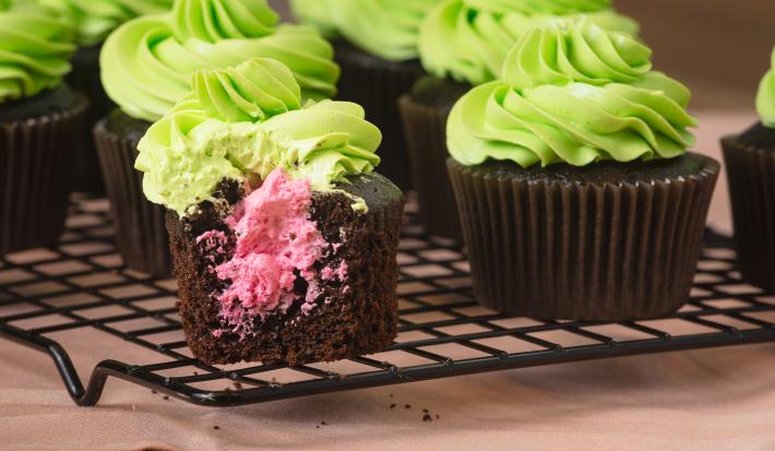 Imagem de cupcakes de chocolate com cobertura verde e recheio rosa.