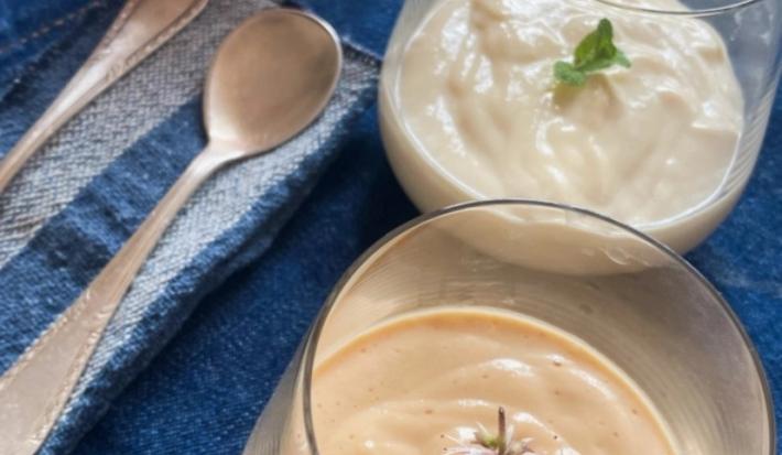 Foto da Receita de Mousse Clássico de Pitanga e Cupuaçu. Observa-se duas taças de vidro transparentes com a mousse sobre um jogo americano azul marinho e duas colheres ao lado, em um guardanapo de pano listrado.