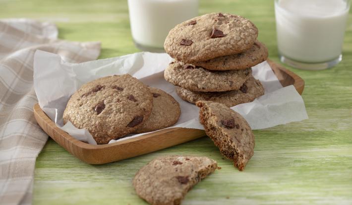 Foto da receita de Cookie Vegano. Observa-se 7 cookies dispostos em uma tábua de madeira, sendo que um está cortado ao meio.