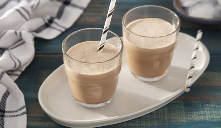 Foto em tons claros de marrom e branco da receita de mocha refrescante servida em duas porções em copos de vidro com canudos listrados sobre uma base de porcelana branca. Ao lado há um pano quadriculado branco e preto