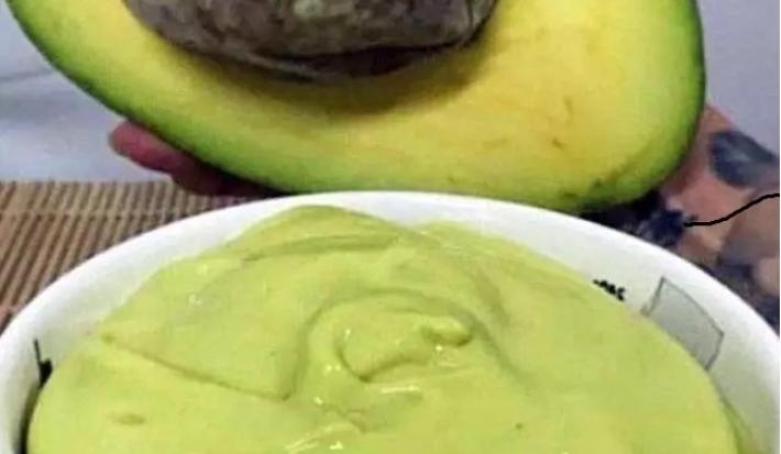 Foto da receita de Mousse de Abacate. Observa-se um potinho branco com a mousse cremosa dentro e um abacate pela metade atrás ilustrando.