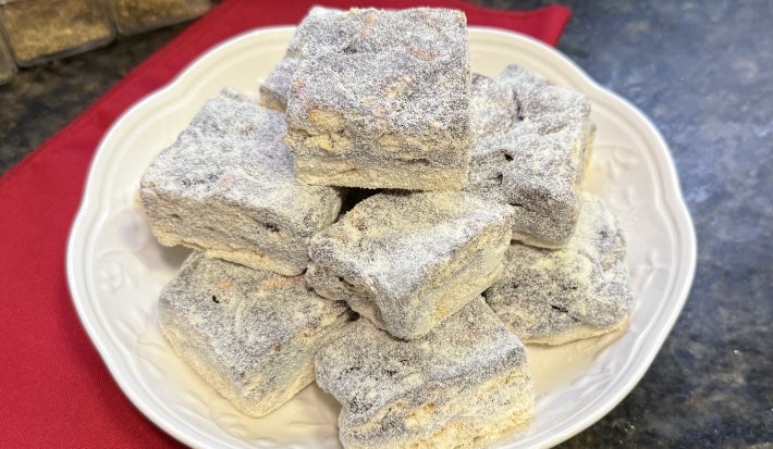 Foto aproximada da receita de Palha Italiana Dois Amores, servida em pedaços um sobre o outro, em um prato branco numa bancada de mármore com um tecido vermelho