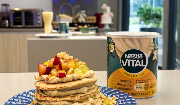 Fotografia em tons de azul e amarelo em uma bancada de cozinha com um prato azul ao centro e panquecas com creme e frutas em cima.