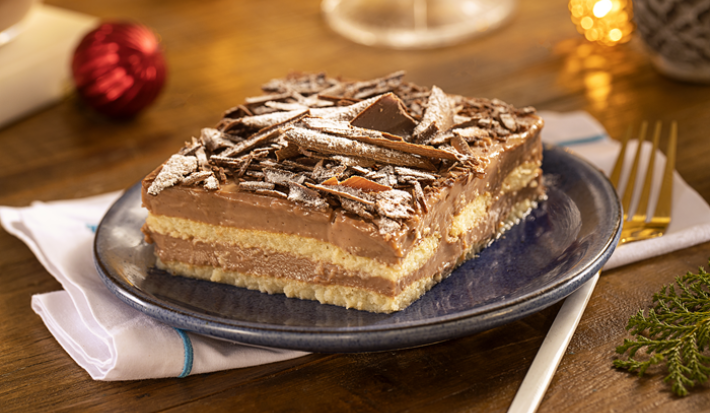 Fotografia mostra um um pavê de chocolate servido em um prato de sobremesa, com suas camadas de chocolate cremoso e biscoito perfeitamente visíveis.