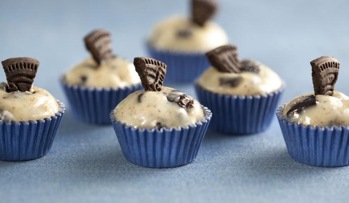 Fotografia em tons de azul e bege, mostrando seis docinhos decorados com pedaços de biscoito e tudo sobre bancada na cor azul.
