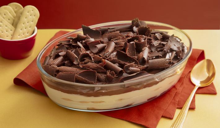 Foto da receita de Torta Alemã. Observa-se um refratário de vidro transparente com a torta decorada de raspas de limão sobre um guardanapo de pano vermelho.