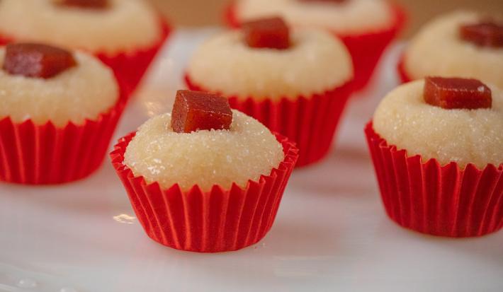 Fotografia de sete unidades de forminhas vermelhas com brigadeiro de romeu e julieta. Por cima de cada um tem um quadradinho de goiabada, e todos estão sobre um apoio decorativo de cor branca.