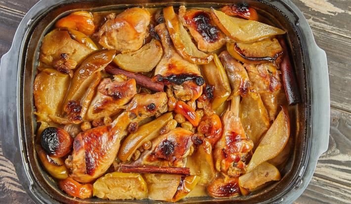 Fotografia em tons de marrom com uma travessa ao centro. Dentro da travessa existe pedaços de coxa e sobrecoxa de frango glaceadas com miniperas.