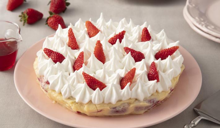 Imagem de uma torta coberta com merengue e decorada com morangos sobre um prato rosa claro.