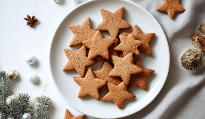 Em cima de uma mesa decoradas enfeites de Natal, prato com biscoitos em formato de estrelas simples.