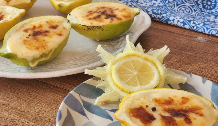 Foto em tons de amarelo da receita de limão brullée servida em três porções divididas em dois pratos decorados sobre uma mesa de madeira com um pano azul ao fundo