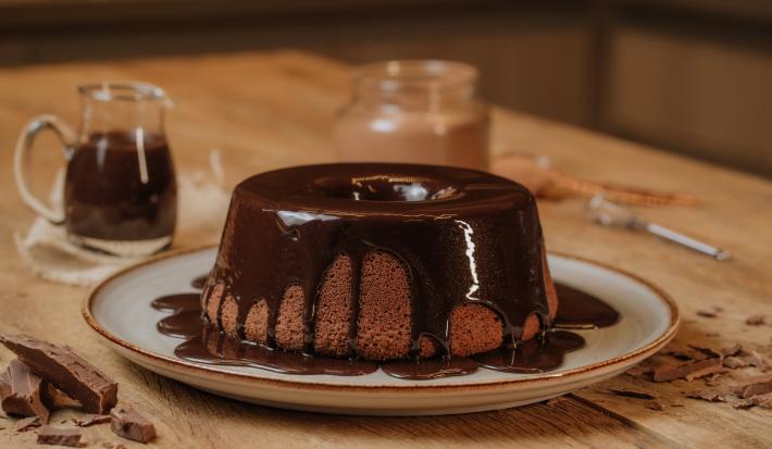 Imagem de um prato sobre uma bancada de madeira com um bolo de chocolate com calda de chocolate.