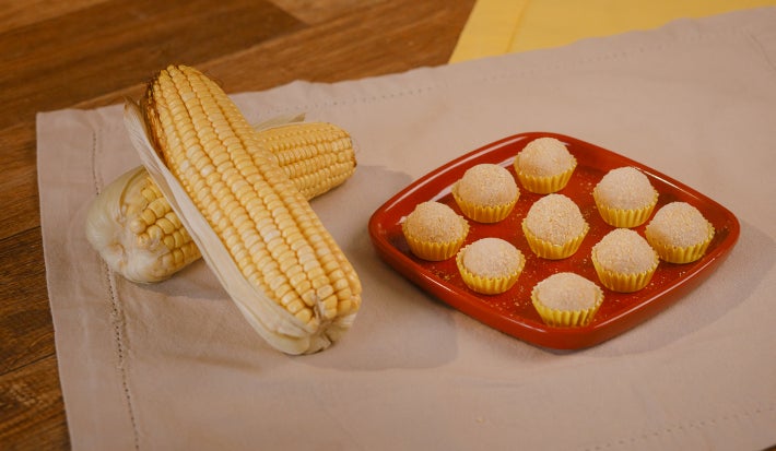 brigadeiros da farinha láctea sob prato vermelho ao lado de espigas de milho