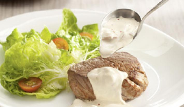 foto tirada de um prato redondo branco com um medalhão de filé com creme por cima e ao lado folhas de alface