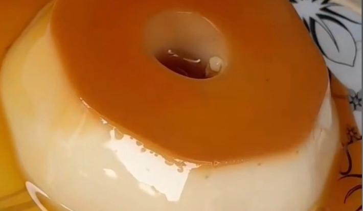 Fotografia de um mini pudim com calda sobre um prato branco com desenhos de cor preta.