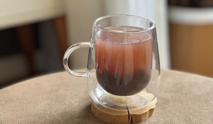Foto da receita de Bubble Tea Caseiro, servido em uma xícara de vidro transparente, sobre uma pequena base de madeira em uma mesa