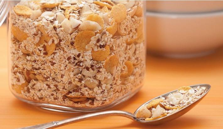 fotografia em tons de marrom tirada de uma bancada marrom vista de frente, contém um pote transparente com granola.