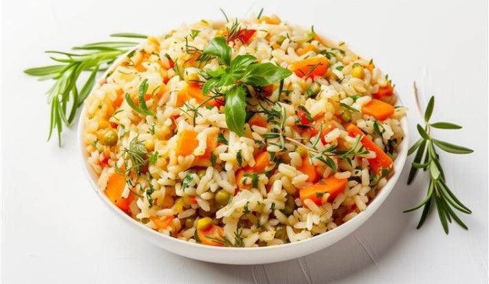 Visto de cima, prato branco redondo com arroz soltinho, cenouras cortadas em cubos, ervilhas e pedaços de cheiro-verde picados.