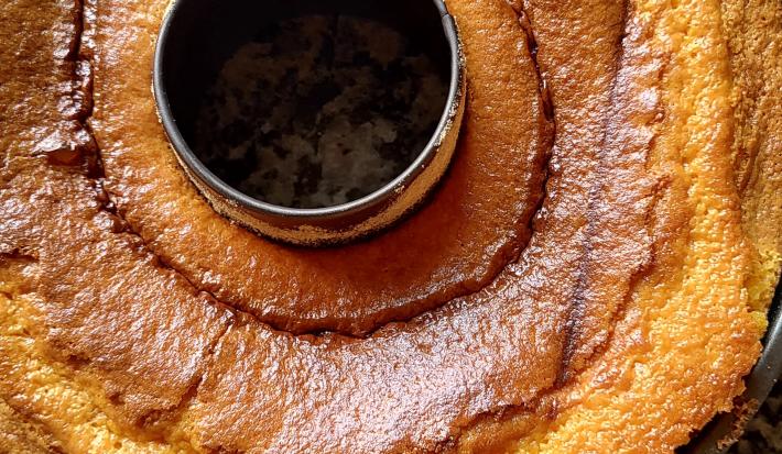 Fotografia de uma forma de bolo preta com furo central com um bolo de cenoura brilhante sobre uma bancada.