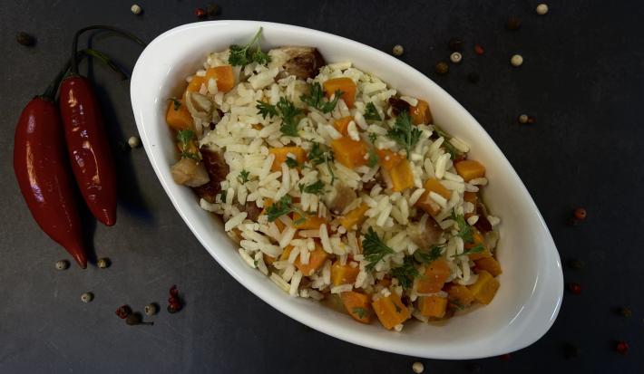 Foto vista de cima da receita de Arroz com Bacon e Cenoura, servido em um refratário de vidro branco, em uma bancada decorada com duas pimentas dedo-de-moça