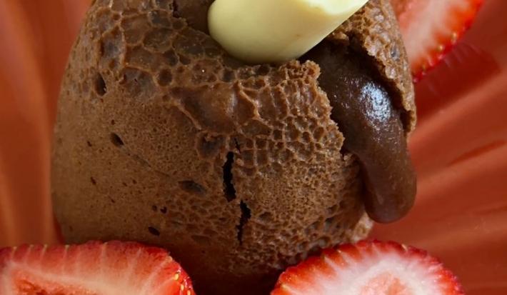 Fotografia de um petit gateau de chocolate com baton duo em um prato vermelho fundo com morangos.