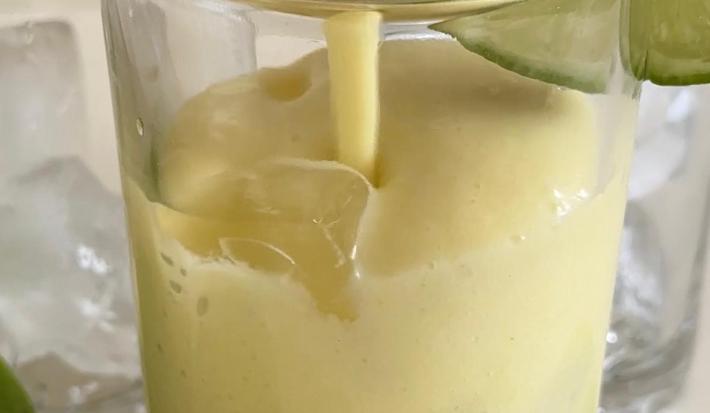 Fotografia em tons claros de um copo de vidro com limonada alemã, com gelos e uma fatia de limão decorando o copo.