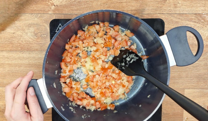 Tomates, cebola e alho refogando em panela sobre fogão portátil preto