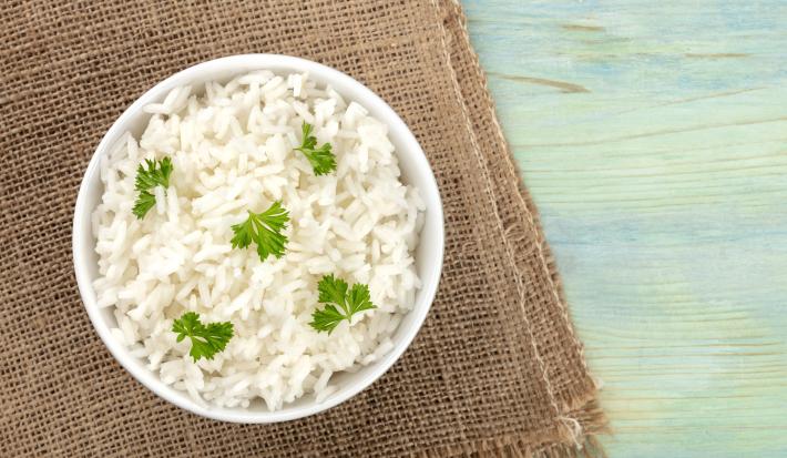 fotografia em tons de azul, marrom e branco de uma bancada azul vista de cima. Contém um pano marrom ao lado esquerdo, por cima um recipiente redondo branco com arroz e salsa.