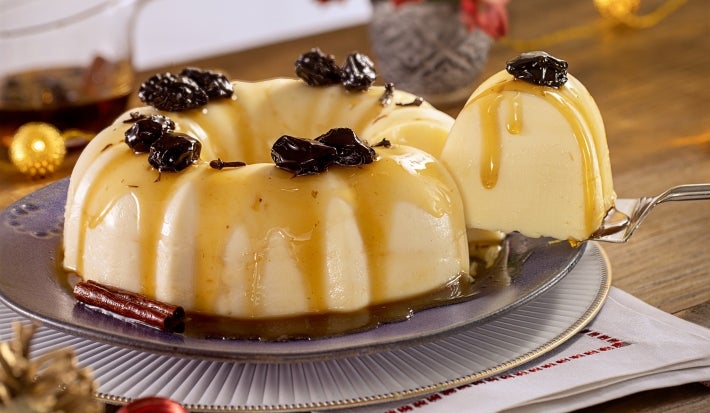 Imagem de um prato com a receita de manjar com calda de ameixa e uma espátula tirando um pedaço.
