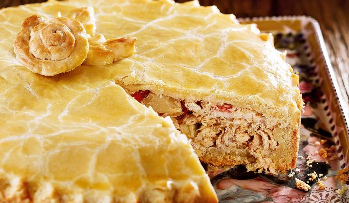 Foto de uma torta de frango com uma fatia a menos em cima de um prato decorado