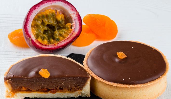 Fotografia de duas minitortinhas de maracujá com chocolate sobre um apoio pequeno preto quadrado.