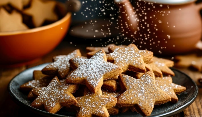 Em cima de uma mesa, prato redondo preto com biscoitos em formato de estrelas, polvilhado com açúcar de confeiteiro.