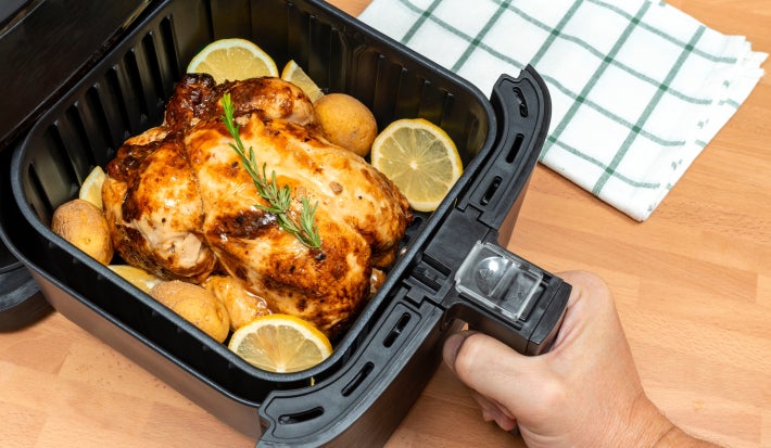 Imagem de uma air fryer com um chester dentro com rodelas de limão e um ramo de alecrim.
