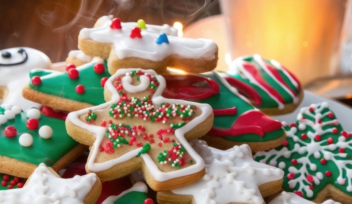 Em cima de uma mesa, prato redondo com biscoitos em formato de estrelas e árvore de Natal, decorados com glacê colorido e confeitos coloridos na cores vermelho, verde e branco.