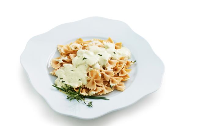 Fotografia em tons de amarelo em um fundo branco com um prato raso branco ao centro e o macarrão ao creme de ricota e ervas dentro.