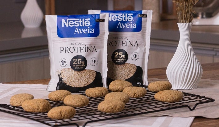 Receita de cookies proteicos servidos em uma grade sobre uma mesa de madeira com embalagens de Nestlé Aveia Proteína