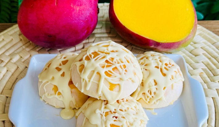 Fotografia mostra bombons de manga cobertas de chocolate branco. No mesmo cenário há duas mangas, sendo uma metade aberta.