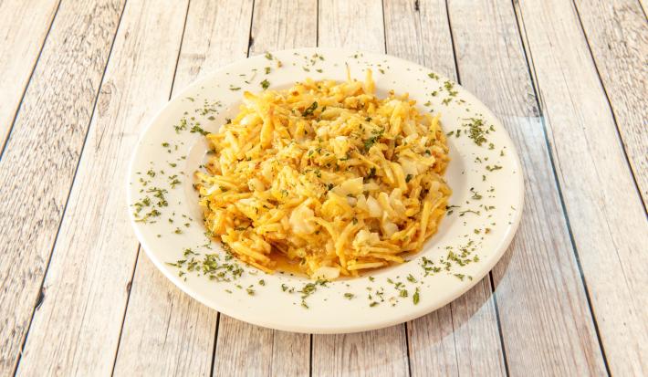 Fotografia de um bacalhau desfiado gratinado com batata palha, ovos batidos e requeijão. O bacalhau está em um prato branco fundo com salsinha picada e salpicada.