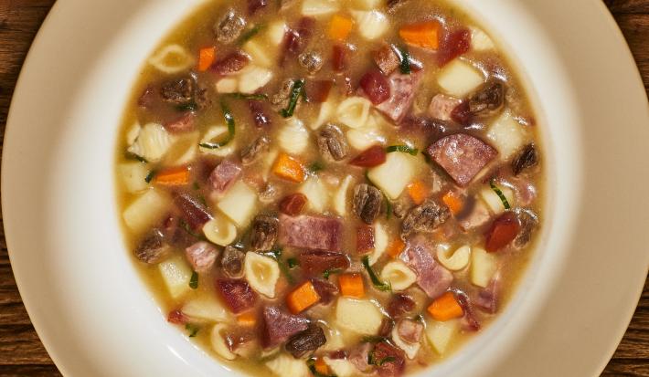 Foto bem aproximada de um prato branco fundo no qual está a receita pronta de sopão de carne com legumes e linguiça